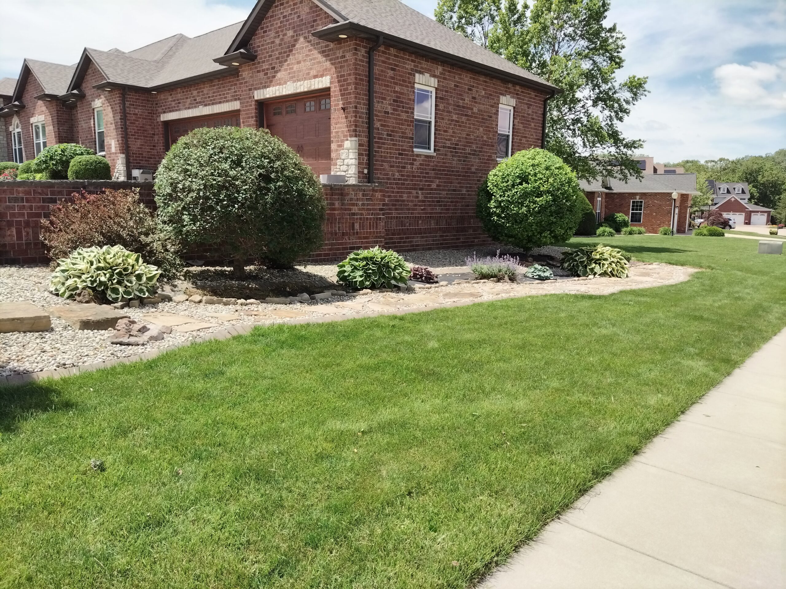 A brick home with a well-maintained lawn and neatly trimmed shrubs in the front yard.