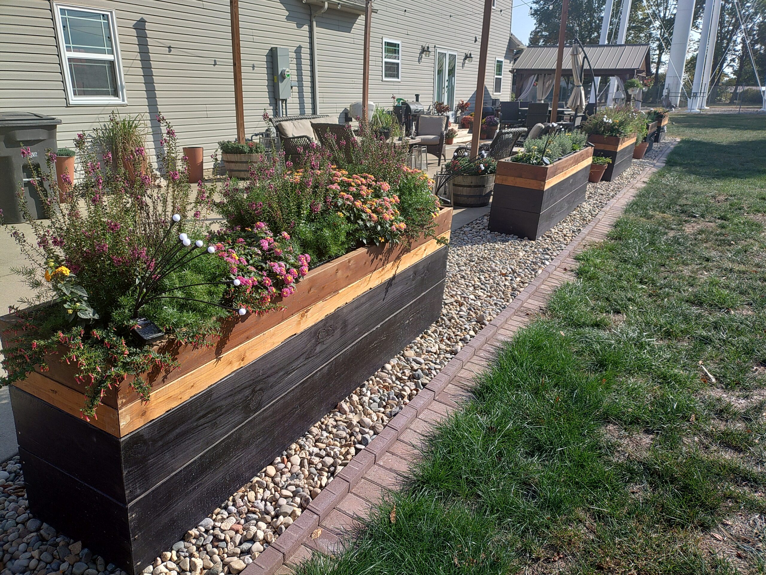 A row of colorful flower boxes arranged neatly in a well-maintained yard, showcasing various blooming plants.