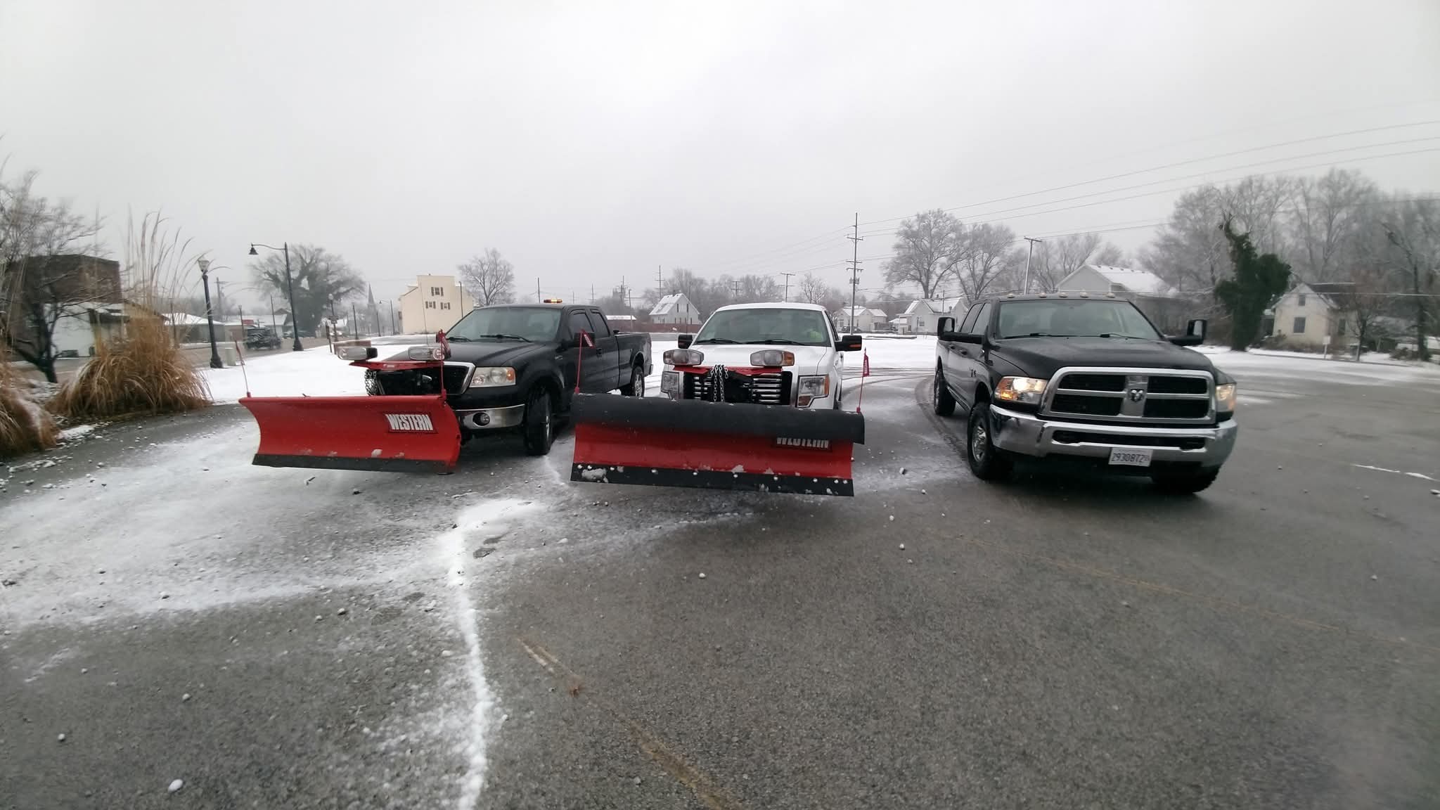 Three snow plows parked in a parking lot, ready for winter weather operations.