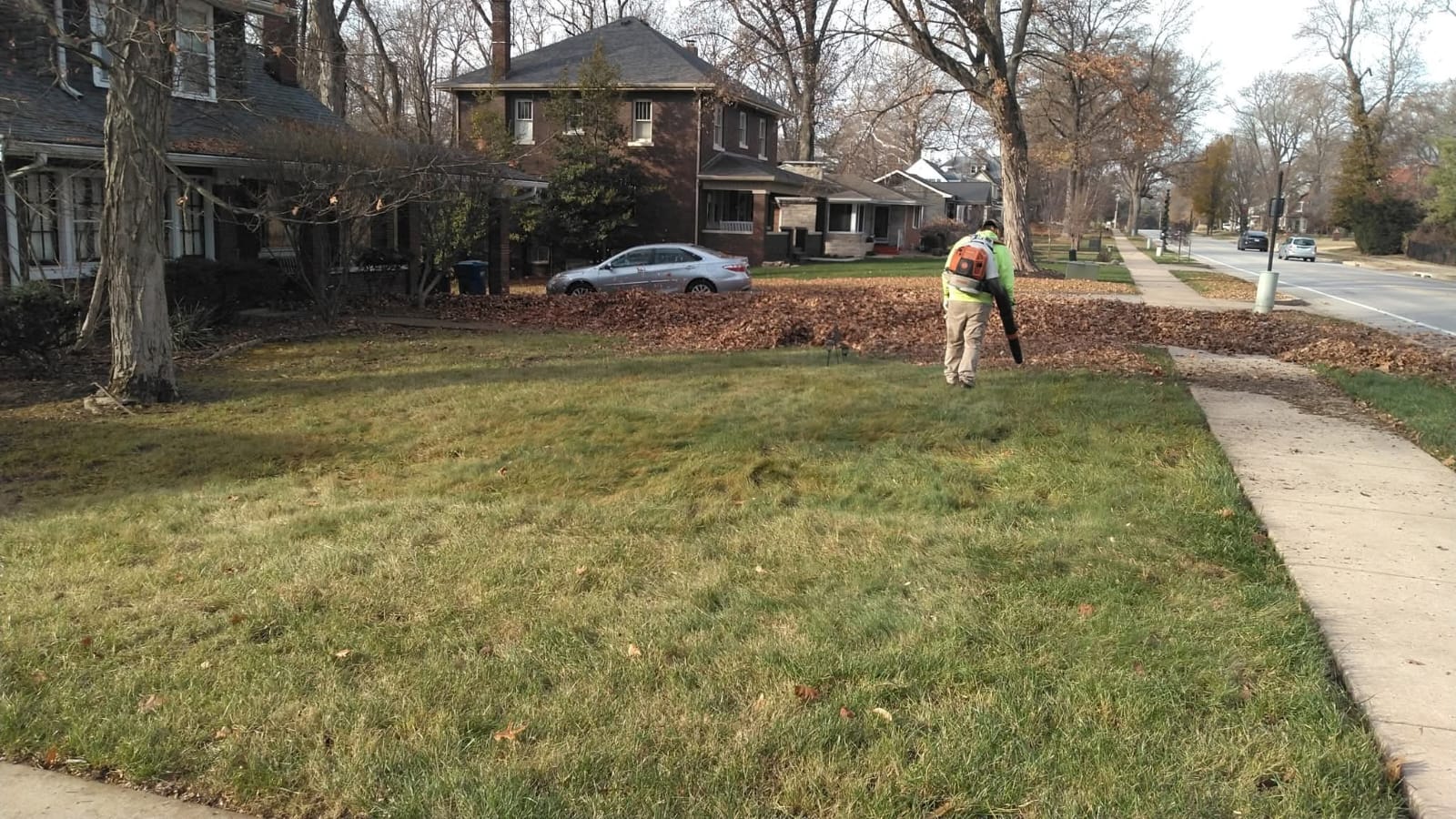 A man using a lawn mower to cut grass in a residential neighborhood, surrounded by houses and greenery.