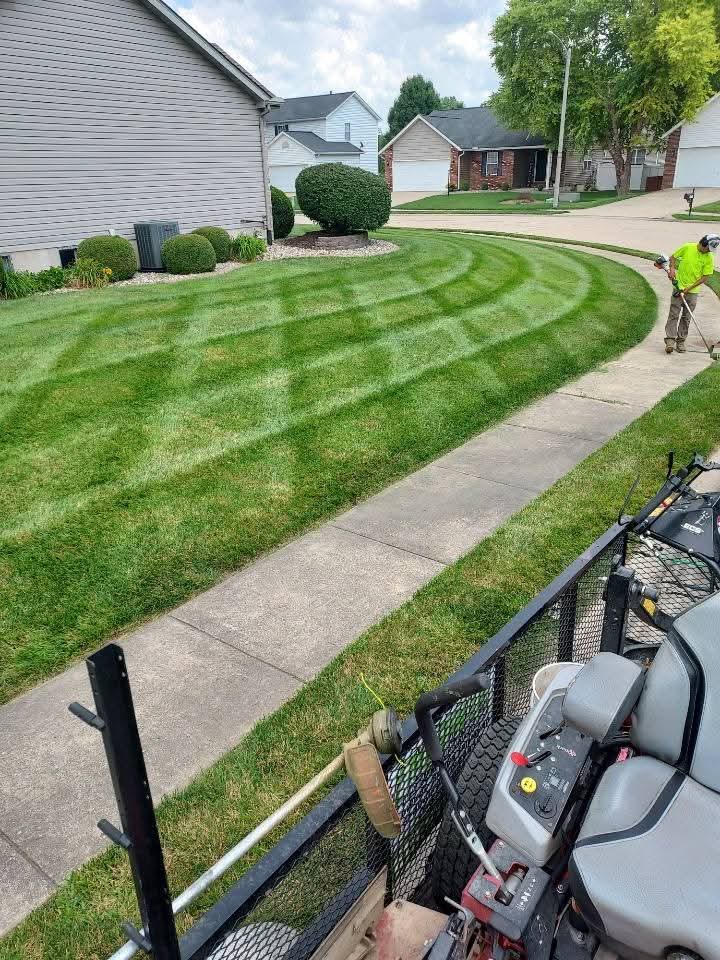 A person operates a lawn mower, trimming the grass in a well-maintained yard.
