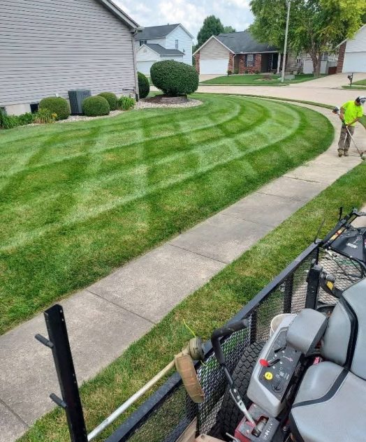 A person operates a lawn mower, trimming the grass in a well-maintained yard.